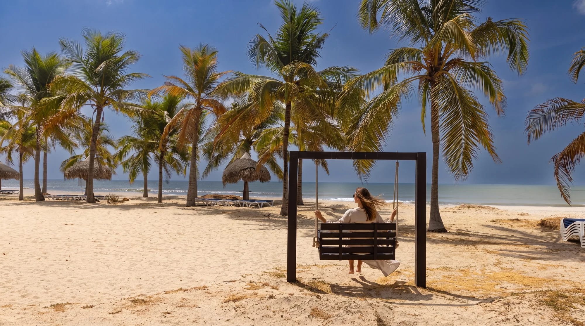 Mujer sentada en un columpio frente al mar, entre palmeras